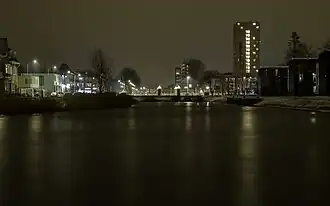 Het Oosterhamrikkanaal vanaf het Ebbingekwartier bij avond. Rechtsachter De Groenling. Middenachter de dam door het kanaal met erachter de Kapteynbrug. Rechtsachter de Kapteynbrug de Wielewaalflat.
