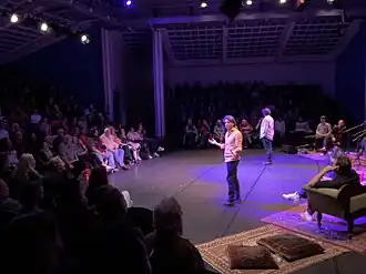 Wijde foto van een theaterzaal met twee vertellers en publiek