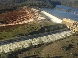 De Oroville Dam in februari 2017. Op de voorgrond de betonnen overlaat en daarachter stroomt het water over de snel eroderende noodoverlaat.
