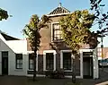 Huis met topgevel, van eenvoudige doch harmonische architectuur, goede proportie's. Specifieke stedebouwkundige ligging