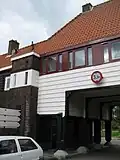 Poortgebouw met twee winkels met bovenwoningen, met veel hout zoals de zware kolommen in poort, bouwstijl Amsterdamse School, ligging aan Purmerweg centraal deel van Tuindorp Nieuwendam