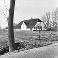 Gepleisterde boerderij, onder rieten wolfdak. Rechts een opkamer. Vensters met luiken en schuiframen met goede roedenverdeling