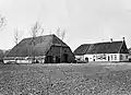 Boerderij van het Noord-Brabantse langgeveltype, met topgevel aan de kop van het woonhuis, waarover zadeldak met pannen, rieten wolfdak over de stal; witgepleisterde gevels waarin zesdelige schuiframen; in de kopgevel jaarankers. Afzonderlijke schuur van het Vlaamse type met rieten wolfdak waaraan voet van pannen, en met bakstenen wanden