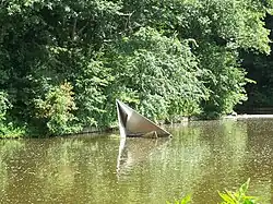 Roestvaststalen object met keien. Stelt opgevouwen papieren bootje voor. (1977) (genomen in 2012)