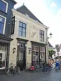 Huis met schilddak en gepleisterde lijstgevels en versierde ingangspartij aan beide zijden, met Korinthische pilasters en guirlandes in het hoofdgestel