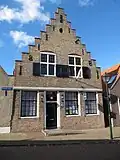 Huis met trapgevel. Sierankers. Na de oorlog geheel vernieuwd. Boven: houten kruisramen. Beneden: puibalk, ramen 18e-eeuws