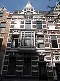 Herenhuis in neorenaissance trant, gedateerd in cartouches in de ontlastingsbogen. Middentopgevel met rolwerkvoluten, obelisken en aedicula. Versiering met banden. Houten erker op voluutconsoles