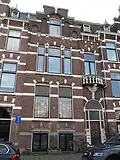 Pand in neorenaissance trant met trapgevel, waarin ontlastingsbogen, blokken en banden. Rechts een terugliggende ingangspartij met boogfries en balcon met balustrade