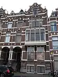 Pand in neorenaissance trant met rechts topgevel. Brede houten erker op korbelen. Gevelversiering met banden en blokken. Links getoogde ingangspartij