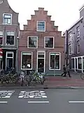 Pand met brede trapgevel met getande horizontale lijst, bogen boven de ramen, gevel met dodekop geverfd, benedendeel intact