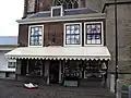 Huis tegen de grote kerk aan gebouwd met rechte kroonlijst, leien dakbedekking, kleine roeden in schuiframen