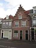 Pand met gepleisterde trapgevel met ontlastingsbogen boven de vensters, midden pinakeltop rustend op console met gebeeldhouwde kop 1e helft 17e eeuw