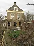Huis van begane-grond en verdieping met schilddak, dat achter tegen een puntgevel aansluit en een topschoorsteen draagt.