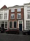 Huis met eenvoudige Empire lijstgevel, geelgepleisterd, ingang omlijst door geblokte pilasters en kroonlijstje met triglyphen, druppen en tandlijst in het deurkalf