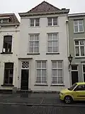 Huis met gebosseerd gepleisterde lijstgevel, kroonlijst op klossen en ingang tussen gecanneleerde pilasters. Plat dak