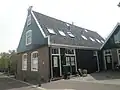 Houten huis met aan de straat een puntgevel met fronton boven een bakstenen pui
