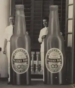Reedijk en Jong Baw naast een fles bier van Handelmaatschappij Van Romondt's (ca. 1935)