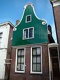 Huis met houten klokgevel boven een pui van baksteen