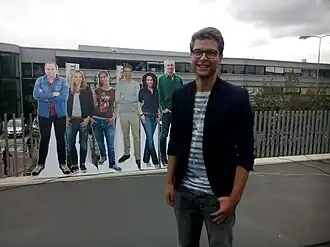 Kammeijer voor het NOS-gebouw in Hilversum in 2015. Op de achtergrond de presentatoren van het Jeugdjournaal.