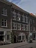 Huis met na 1945 vrijwel vernieuwde lijstgevel, geleed met boognissen en voorzien van een uithangteken in vorm van een bel aan een vogelkop