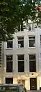 Gepleisterd koopmanshuis met eenvoudige lijstgevel. Onder de kroonlijst liggende vensters, gescheiden door triglyfen