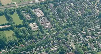 Overzicht van de omgeving. Linksachter sportvelden, schoolgebouwen en de spoorbaan. Op de voorgrond de Oosterweg, daar (rechts) achter Rummerinkhof met zijstraten.