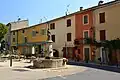 Place de la Fontaine, met fontein en daarachter crème, geel en oranje gestukadoorde huizen