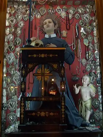 Gerardus Majella zoals hij gebruikelijk wordt afgebeeld: gekleed in een soutane en zijn ogen gericht op een crucifix dat hij in zijn handen houdt.