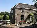 Oorspronkelijke boerderij onder schild- en zadeldaken. Belangrijk door de ligging nabij de Hervormde Kerk