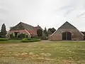 "Schooneveld": boerderij met dwars woonhuis onder pannen schilddak. De vensters voorzien van strekken, roedenverdeling en met luiken behangen. Tussen huis en stal een rond, met riet gedekt voormalig karnhuis. Stal onder met pannen gedekt zadeldak.