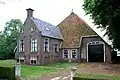 Grote boerderij van het kop-romp type; onderkelderd woongedeelte waarvan zesruitsvensters. Twee schoorstenen met borden. Zandlopervormige beschildering op de inrit. Kleine vensters in het schuurgedeelte