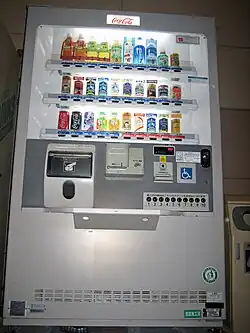 Een frisdrankautomaat in Japan is toegankelijk ingericht met goed bereikbare knoppen op aangepaste hoogte, duidelijke visuele iconen en verlichte productkeuzes, zodat gebruikers met een beperkte reikwijdte of visuele beperking zelfstandig een drankje kunnen selecteren en meenemen.