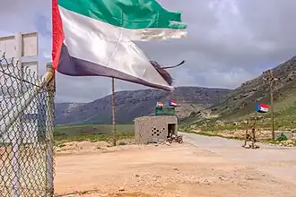 Wegversperring van de Zuidelijke Overgangsraad in het zuiden van Socotra ter bewaking van een benzinestation. Dit benzinestation werd bekostigd door de Emiraten, waarvan de vlag op de voorgrond zichtbaar is.