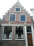 Huis met trapgevel, voorzien van gebeeldhouwde cartouches in het fries