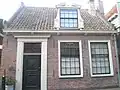 Huis met lage lijstgevel. Ingang met pilasteromlijsting. Dakkapel met gebroken fronton