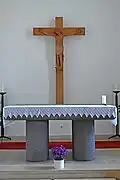 Zicht op het volksaltaar en het houten kruis aan de muur.