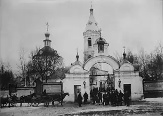 De kerk met klokkentoren en toegangspoort; foto begin 20e eeuw