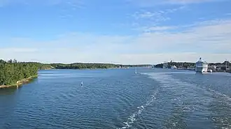 De baai gezien in noordelijke richting. Ter hoogte van het grote schip (rechts) is net wat bebouwing van Mariehamn zichtbaar.