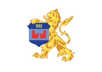 alt=Schild: Azuur met lichtblauwe band, "1933" in goud, en een rood kasteel. Schildhouder: Gouden leeuw