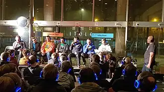 alt=Het Tech45-panel op het podium tijdens het 2e Belgische podcastfestival in Gent. Van links naar rechts: Ruurd Sanders, Jelle D'Hulster, Stefaan Lesage, Davy Buntinx, Steven Op de beeck, Toon van de Putte, Maarten Hendrikx, Floris Daelemans