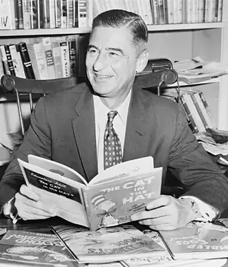 Dr. Seuss omgeven door zijn boeken. Hij houdt zijn bekendste werk, De kat met de hoed, vast.