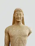 Vooraanzicht van een kouros, die de karakteristieke archaïsche haarstijl toont (Archeologisch Museum, Thebe)