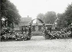 Het borstbeeld rond 1920 met een rozenboog ervoor.