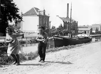 Een vrouw en een man trekken een schuit door een binnenkanaal in Nederland, 1931