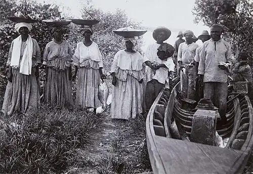 Portret van een groep Creoolse visverkoopsters naast de vissers en hun boot (ca.1915)