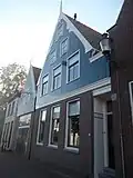 Huis met houten van windveren in accoladevorm voorziene topgevel boven een pui van baksteen