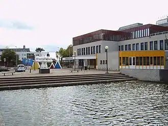 Een gebouw met een pleintje met een kunstwerk ervoor, aan het water