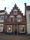 Huis met trapgevel met geblokte ontlastingsbogen, toppilaster, sierankers en schuiframen in stijl