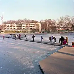Schaatsers op het water van het Kromhoutpark, met uitzicht op de flat aan de Henriëtte Ronnerstraat