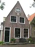 Huis met puntgevel; gebeeldhouwde aanzetstukken; gevelsteen met zeilschip en opschrift OOG IN SEIL. Deur en snijraam